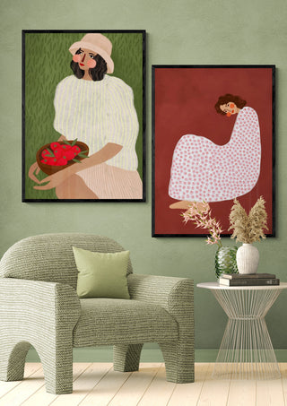 Two framed Sadness - Bea Muller art prints on a green wall above an armchair and side table with decor.
