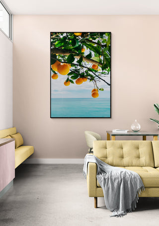 Framed art of Amalfi Coast oranges hanging above a beige sofa in a modern living room with coastal décor.