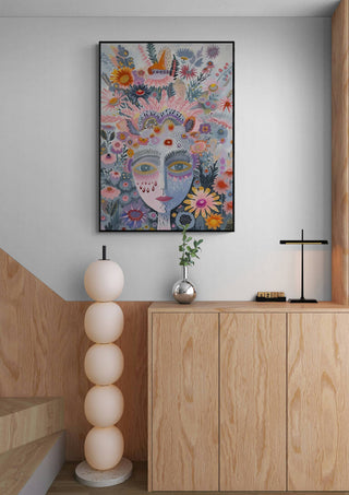 Framed "The Tribe - Vincent V" artwork with floral face design on a modern wood cabinet and neutral interior.