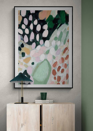 Abstract painting with soft pink, green, and white tones displayed above a light wood cabinet in a modern room.
