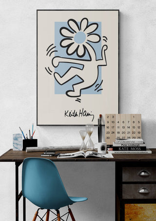 Framed Flowerhead print by Keith Haring hanging above a modern desk with books and office supplies.
